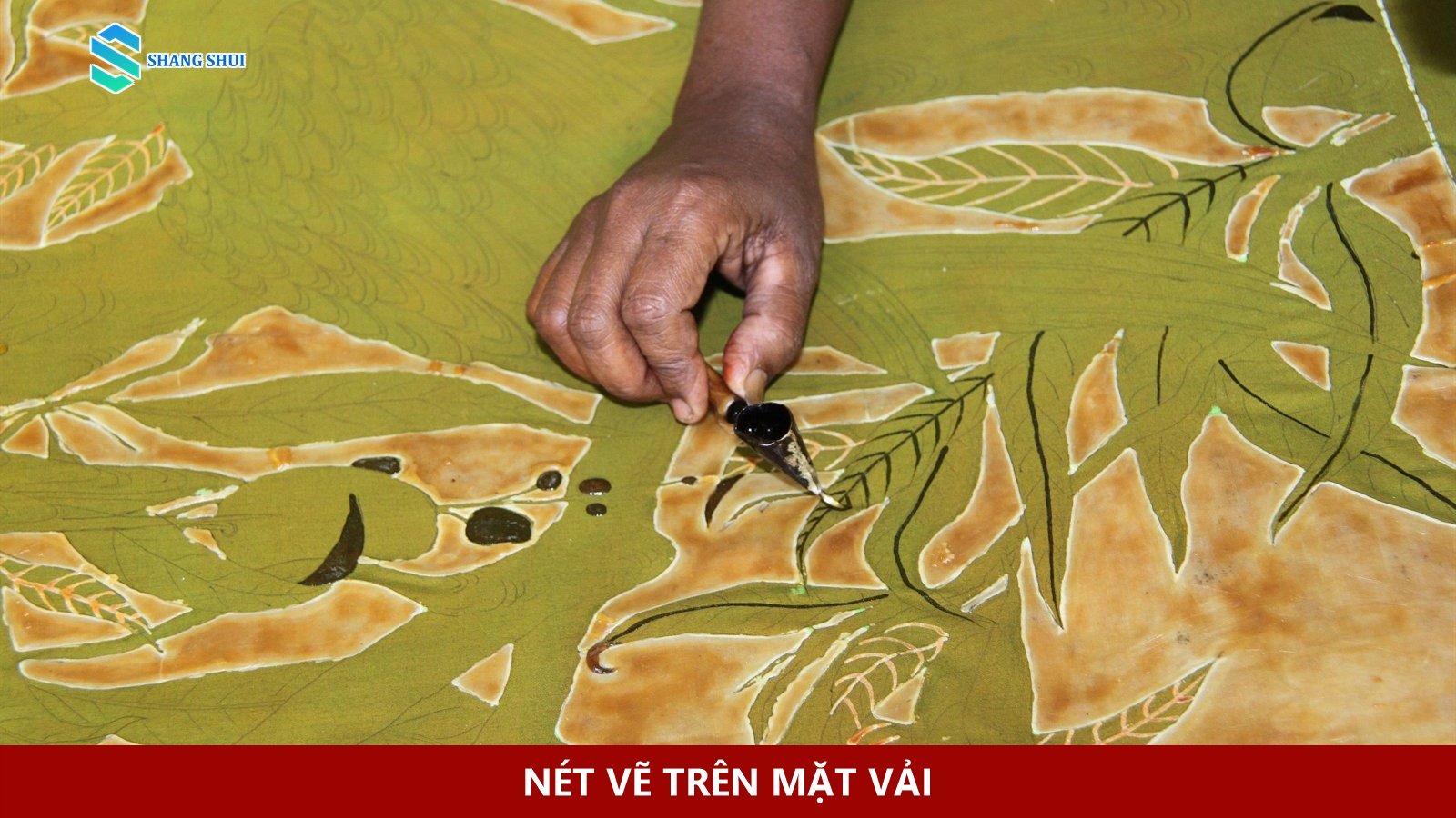 Bàn tay dùng dụng cụ đầu nhỏ tạo nét trên tấm batik màu xanh.