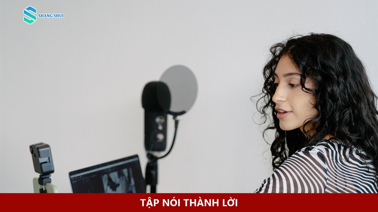 Người phụ nữ nói trước điện thoại đặt trên giá, bên cạnh laptop.