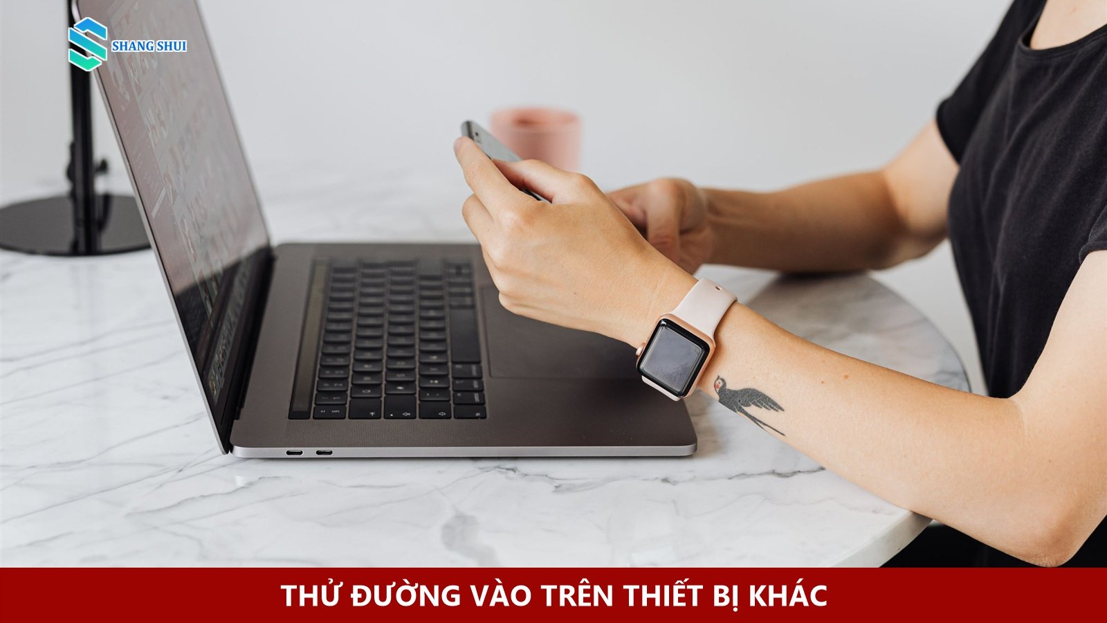 Người cầm điện thoại cạnh laptop trên bàn làm việc.