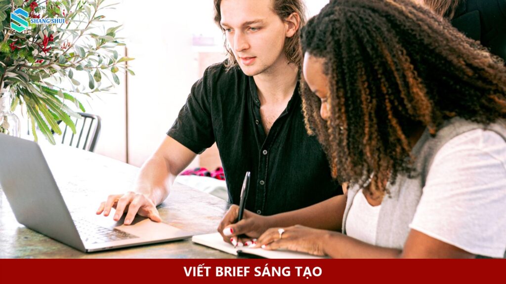 Hai người trao đổi công việc bên laptop và sổ ghi chép