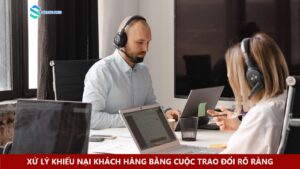 Hai nhân viên đeo tai nghe hỗ trợ khách hàng và trao đổi bên máy tính
